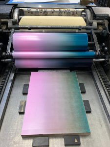Photo of a press and board inked in a gradient from pink to blue