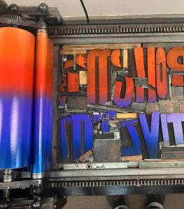 Photo of a press and wood type inked in a gradient from purple to red