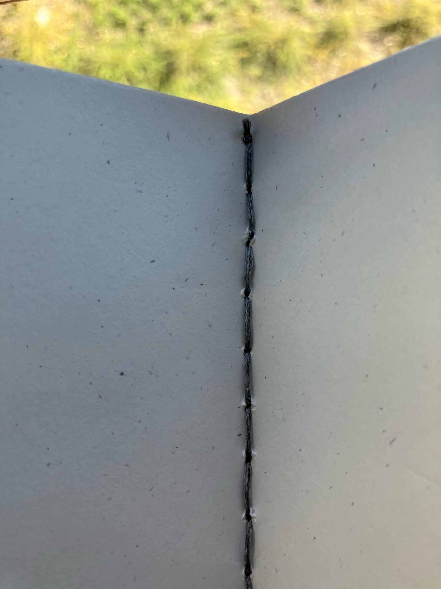 Closeup photo of the inside of a handmade paper-bound journal, showing how the spine is sewn with charcoal thread in a chain stitch that loops back on itself