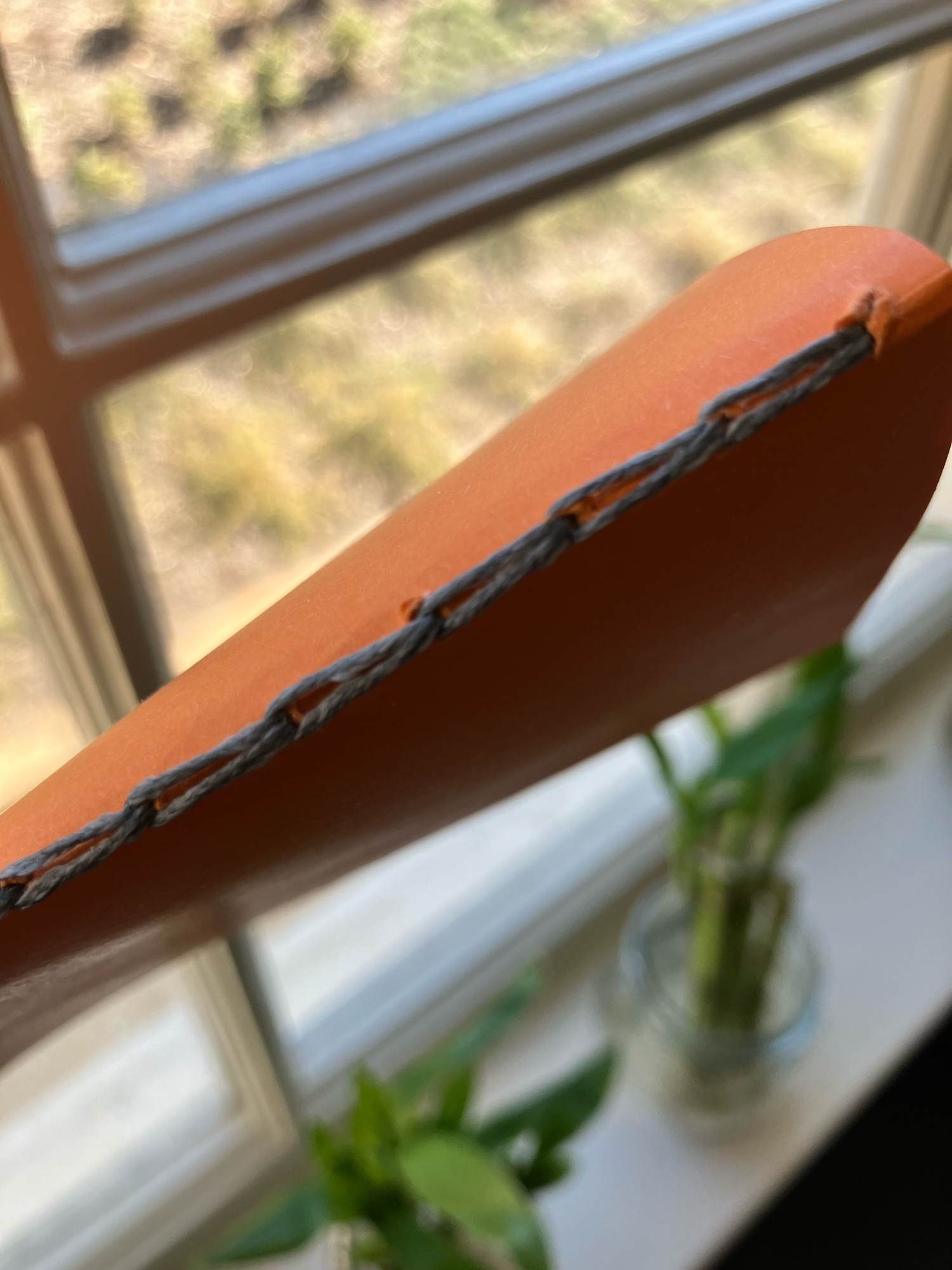 Closeup photo of an orange construction-paper-bound journal, showing how the spine is sewn with charcoal thread in a chain stitch that loops back on itself