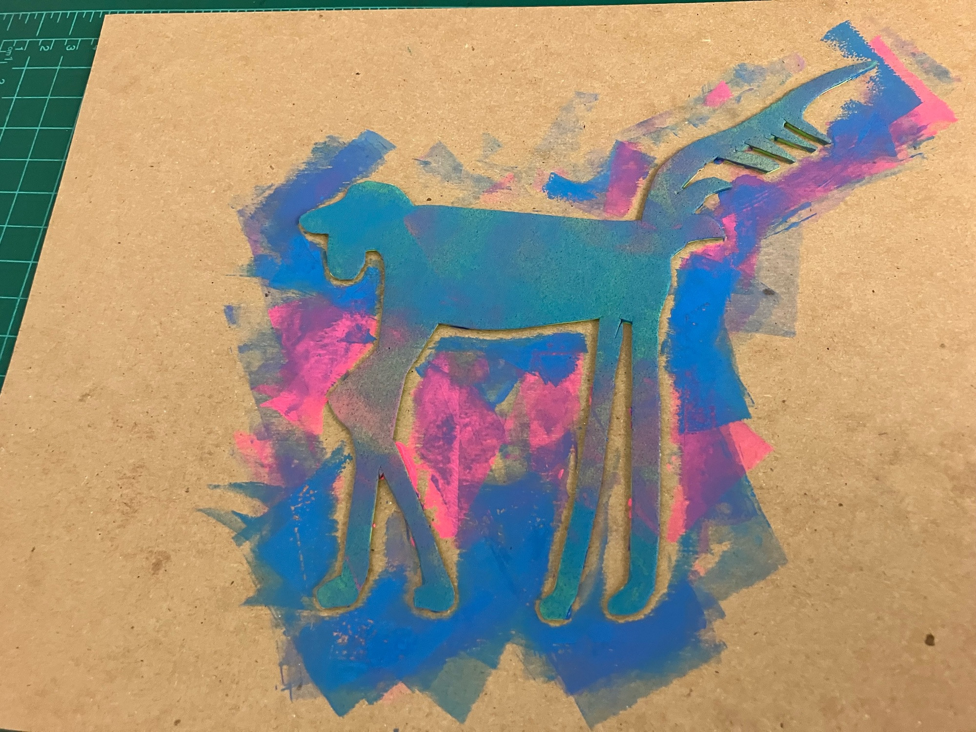 Photo of a tshirt cardboard with a piece of craft foam affixed to it; the craft foam has been cut into the shape of a dog with very very long legs, and inked with fluorescent blue and pink ink.